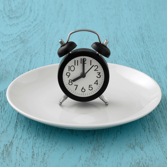 A traditional black alarm clock standing on white dinner table on what appears to be a blue wooden table surface