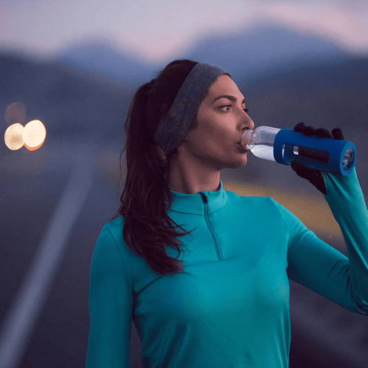 young female athlete standing on the pavement, drinking water and resting after exercising