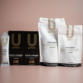 Full product lineup of U Perform supplements, including "active collagen" sachets and boxes, "active greens" powder, and "active berries" capsules, all arranged upright against a soft pink backdrop. The packaging highlights the brand's minimalist design and science-led performance messaging.